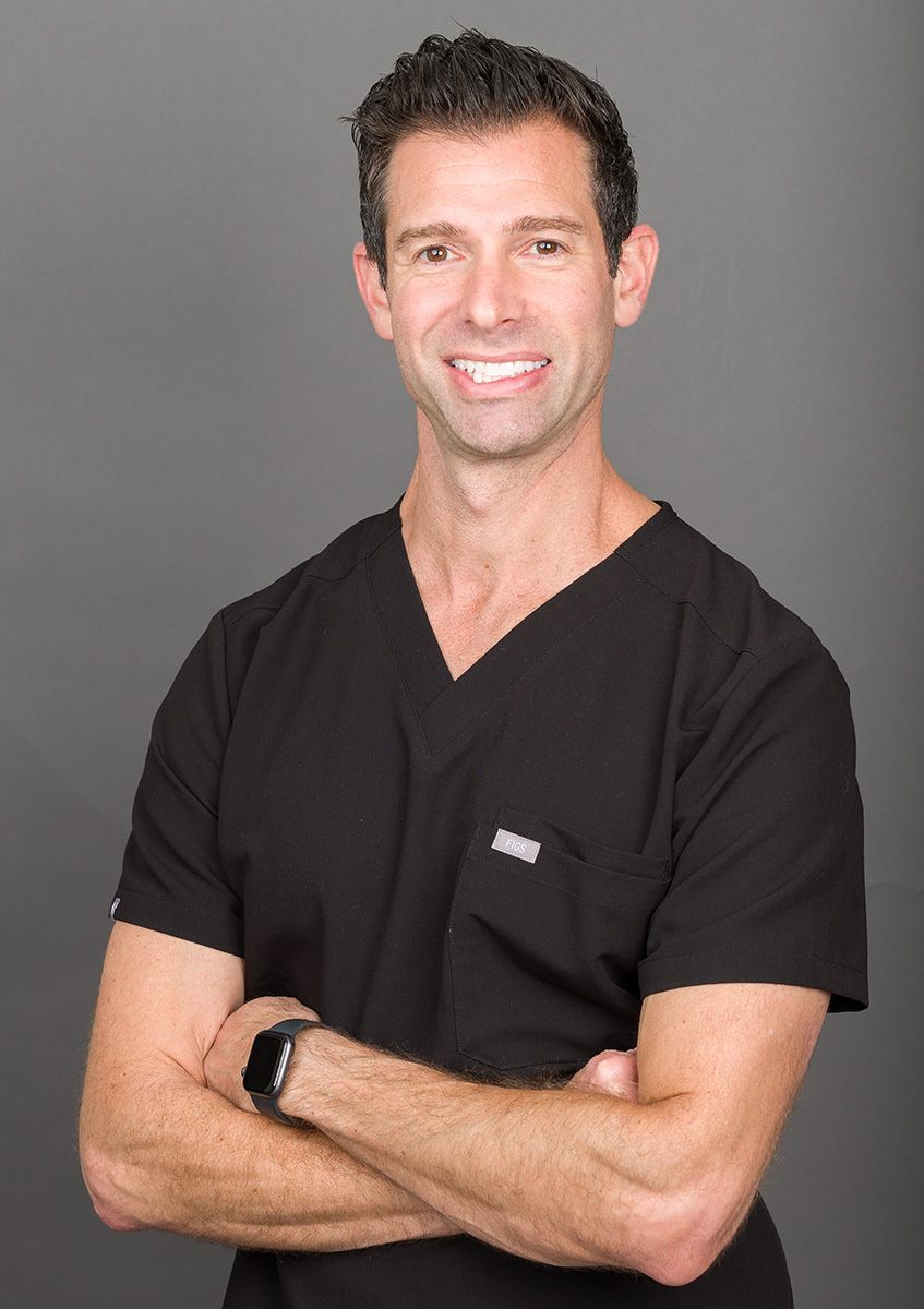 The image shows a man wearing a black shirt with a stethoscope around his neck, standing confidently with arms crossed.