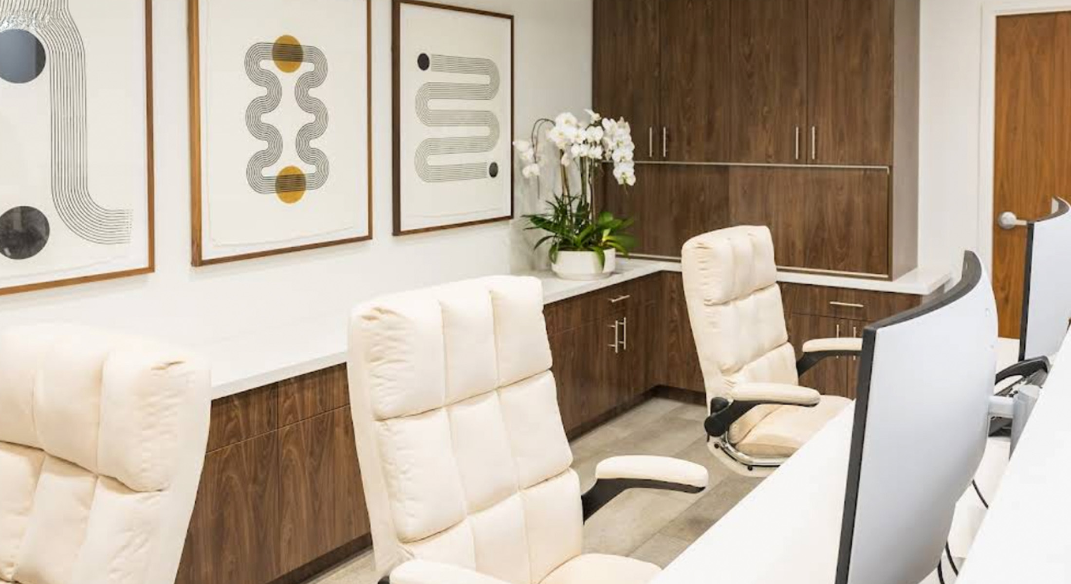 This is a photograph of an interior office space featuring modern furniture, including chairs and desks, with artwork on the walls, a large window, and a well-lit environment.