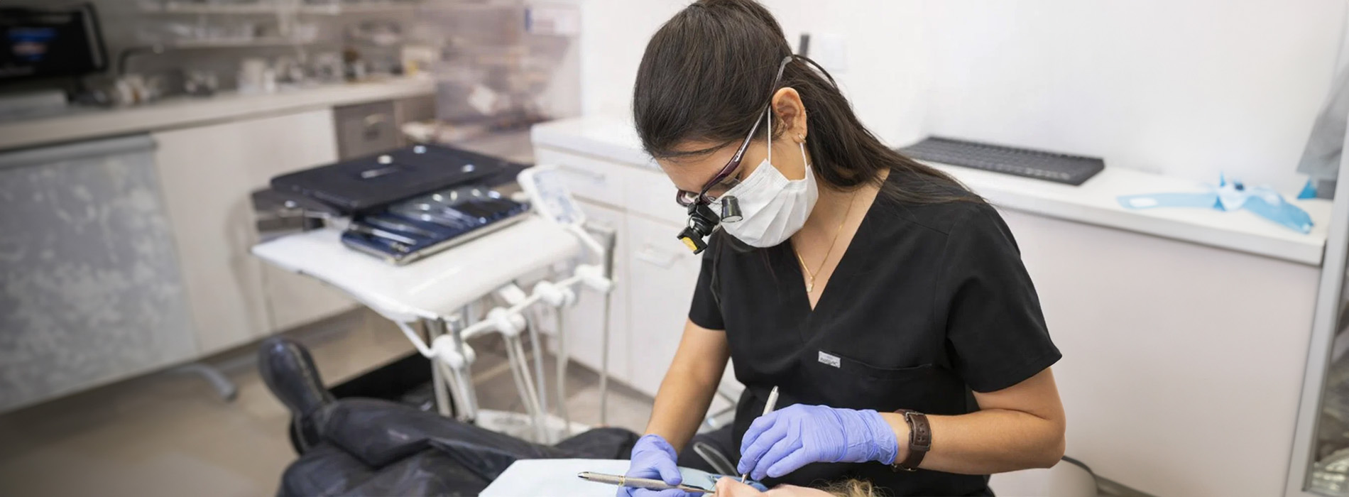 A woman wearing a surgical mask and gloves sits at a desk with papers, working on something.