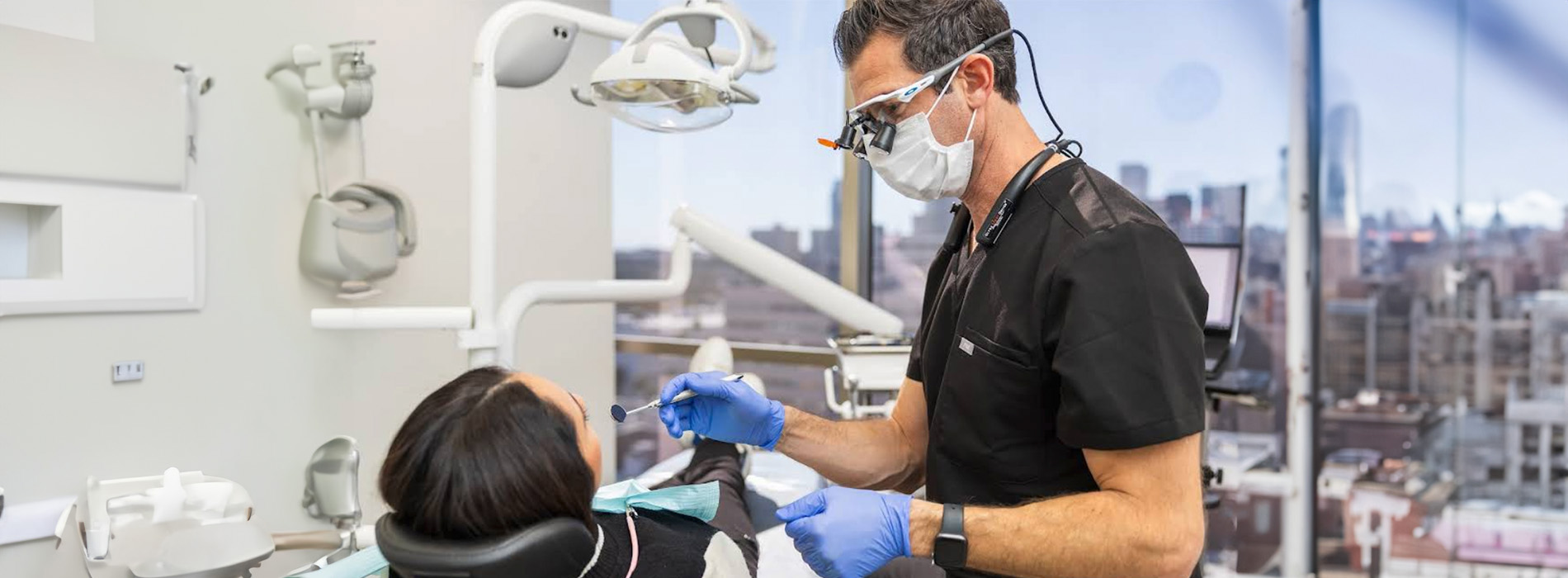 The image shows a dental professional performing oral care on a patient while another person observes.