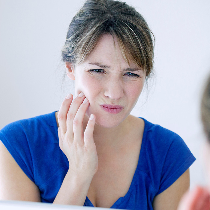 A woman with her hand on her chin, looking at her reflection in the mirror with a concerned expression.