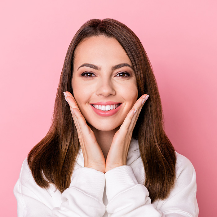 A woman with a smile, wearing a white hoodie, against a pink background.