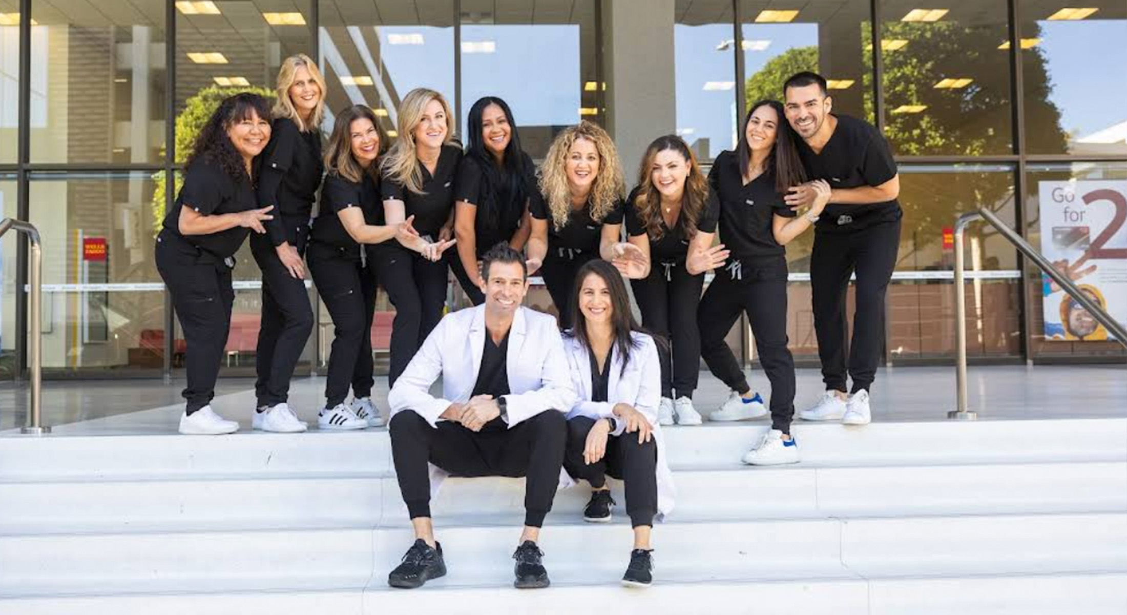 A group of people posing together, likely a team, with some individuals standing on steps in front of a building entrance, smiling at the camera.