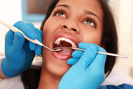 A dental hygienist performing oral care on a patient s teeth while wearing blue gloves and using dental tools.